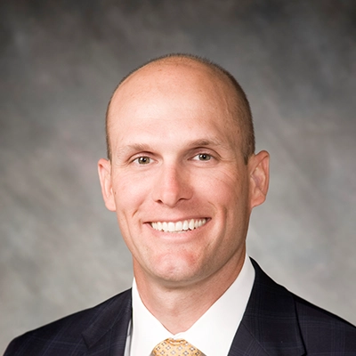 Chiropractor Brett Hoeft Smiling In Front Of Grey Background