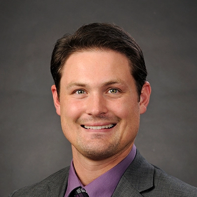 Chiropractor Logan Clarahan Smiling In Front Of Grey Background
